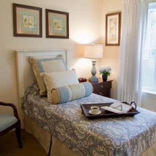 A cozy bedroom with a single bed decorated with pillows and a tray, accompanied by a side table and lamp.