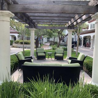 An inviting outdoor seating area under a pergola, surrounded by lush greenery and landscaped gardens.
