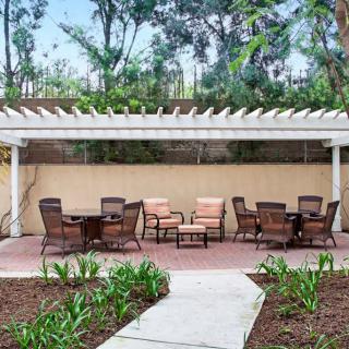 A peaceful garden setting featuring a pergola with outdoor seating and lush greenery.