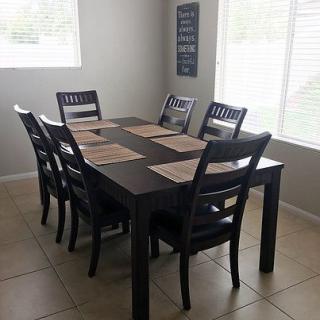 A dining room with a dark wooden table and six chairs, set with placemats near large windows.