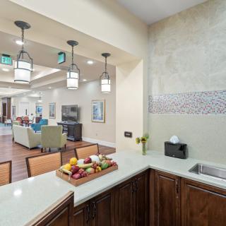 A modern kitchen area opens up to a living space, featuring stylish lighting and a fruit basket on the counter.