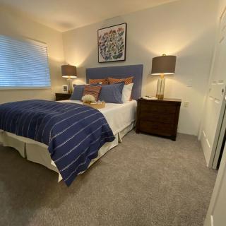 A cozy and modern bedroom with a blue-themed decor, featuring a comfortable bed, two lamps on wooden nightstands, and a decorative painting above the headboard.