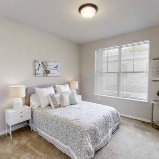 A cozy bedroom with a neatly made bed, flanked by nightstands and lamps, featuring a large window that lets in natural light.