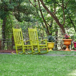 Two bright yellow rocking chairs sit in a lush garden surrounded by trees and potted plants.