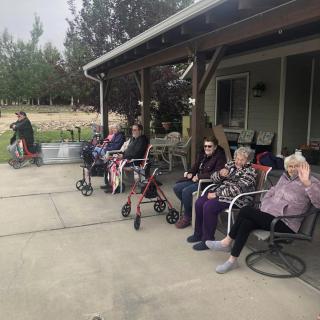 A group of seniors seated and socializing outdoors on a covered patio.