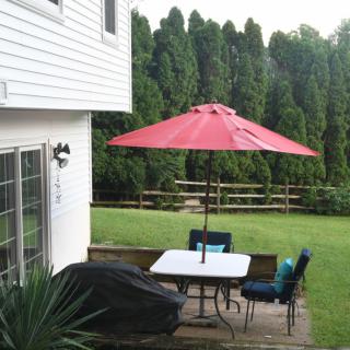 A backyard patio with a table, chairs, and a red umbrella.