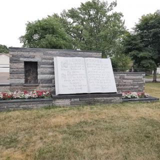 A memorial monument with a wooden structure and plaques, set in a grassy area.
