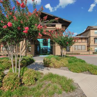 A scenic view of a modern building surrounded by lush landscaping and vibrant flowers under a clear blue sky.