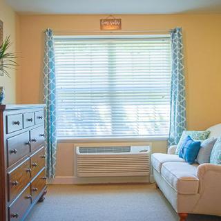 Cozy living room with a sofa, dresser, and large window with blinds and curtains.