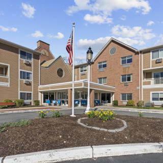 Exterior view of a brick building with an American flag and a landscaped circular driveway.