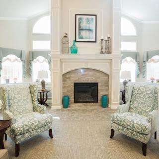 A well-lit living room with patterned armchairs and a decorative fireplace.