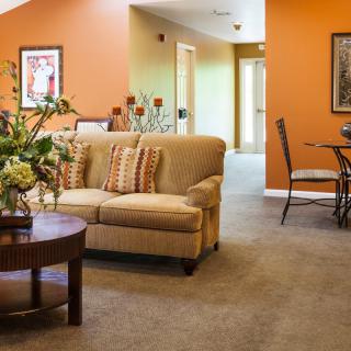A cozy living room with an orange accent wall, featuring a comfortable sofa and a small dining area.