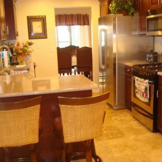 A modern kitchen with a countertop and bar stools, featuring stainless steel appliances and wooden cabinets.