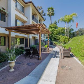 An apartment building with a landscaped patio area featuring a pergola, outdoor seating, and lush greenery.