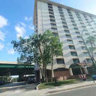 A view of a high-rise residential building under a clear blue sky, accompanied by nearby trees.