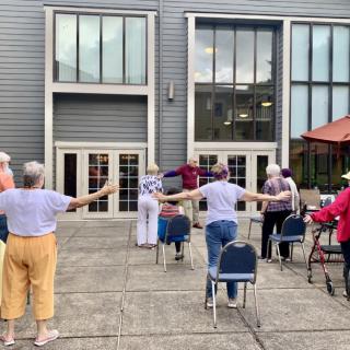 A group of elderly individuals participating in an outdoor exercise session on a patio.