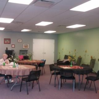 A community room with tables and chairs, decorated with floral arrangements.
