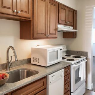 A compact kitchen with wooden cabinets, featuring a microwave, oven, and sink.
