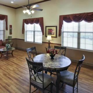 A cozy living and dining area with hardwood floors, featuring a round table and chairs, and large windows allowing natural light to fill the room.