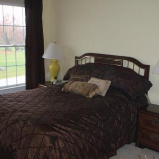 A cozy bedroom with a neatly made bed, pillows, and a lamp by the window.