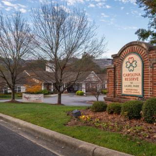 Entrance to a residential area with a brick sign and buildings in the background.