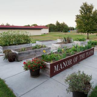 A well-maintained community garden featuring raised vegetable beds at the Manor of the Plains, surrounded by greenery.