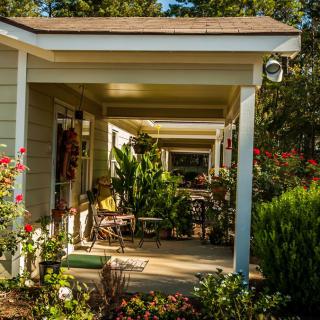 A cozy porch with outdoor seating, surrounded by lush plants and vibrant flowers.