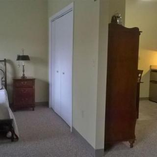 A cozy bedroom featuring a bed, wardrobe, nightstand with a lamp, and a closet.