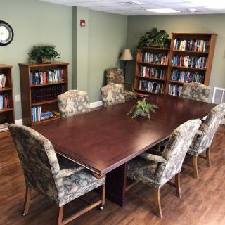 A conference room with a meeting table surrounded by chairs, flanked by bookshelves stocked with books.