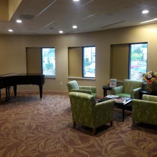 A cozy lobby featuring a piano, green chairs, and natural light from the windows.