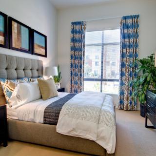A modern bedroom with stylish decor, featuring a plush bed, vibrant curtains, and natural light streaming through a large window.