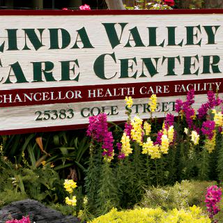 A sign for 'Linda Valley Care Center' surrounded by a garden with colorful flowers.