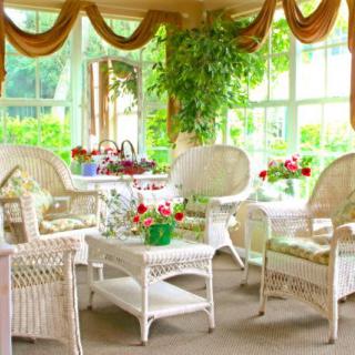 A bright and cozy sunroom featuring wicker furniture and lush indoor plants.