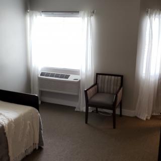 A minimalist bedroom interior with a bed, chair, and bright windows.