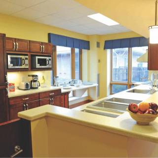 A modern kitchen with wooden cabinetry, large windows, and various appliances.