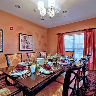A well-decorated dining room with a set table, featuring elegant chairs, a chandelier, and colorful curtains.