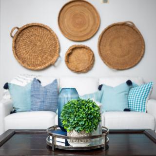 A cozy living room featuring a white couch with blue pillows, adorned with wicker baskets as wall art and a coffee table centerpiece with green foliage.