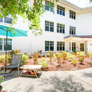 A sunny courtyard with a landscaped garden and seating area in front of a residential building.
