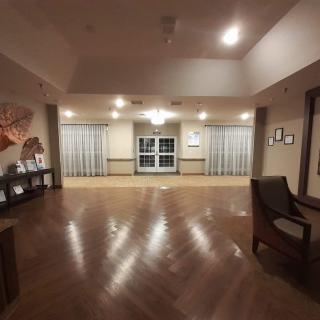 An empty room with wooden floors, featuring chairs along the sides, curtains on the windows, and ceiling lights illuminating the space.