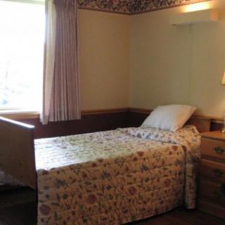 A simple bedroom with a single bed by the window, featuring floral bedding and curtains.