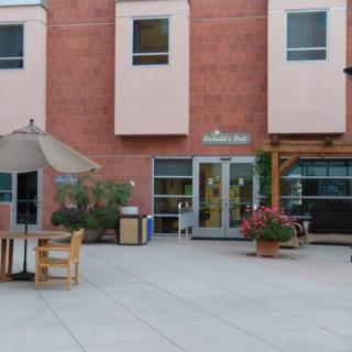 An outdoor patio area with tables, chairs, and a large umbrella in front of a building.