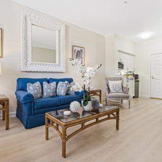 A modern living room featuring a blue sofa with decorative pillows, a stylish coffee table, and elegant decor including artwork and a large mirror.
