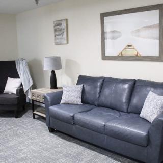 A cozy living room with a blue sofa, an armchair, artwork on the wall, and a lamp on a side table.