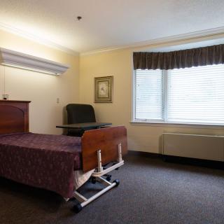 A simple, well-lit room with a hospital bed and a chair next to a window.