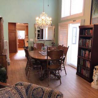 A cozy dining room with a wooden table and chandelier, alongside a bookshelf and large windows.