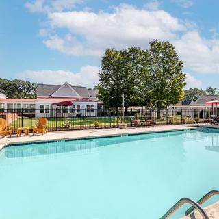 A tranquil outdoor swimming pool in a residential area, surrounded by trees and buildings under a partly cloudy sky.