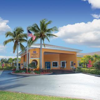 A vibrant building surrounded by palm trees under a clear blue sky with fluffy clouds.
