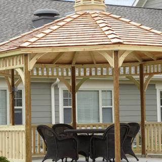 A wooden gazebo with patio furniture underneath, situated in a yard.