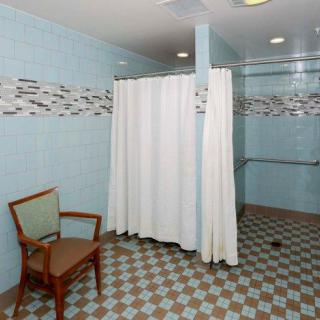 A bathroom with a shower area, featuring a curtain and a chair beside, with tiled walls.