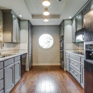 A modern kitchen with sleek cabinets, wood flooring, and a distinctive round window.